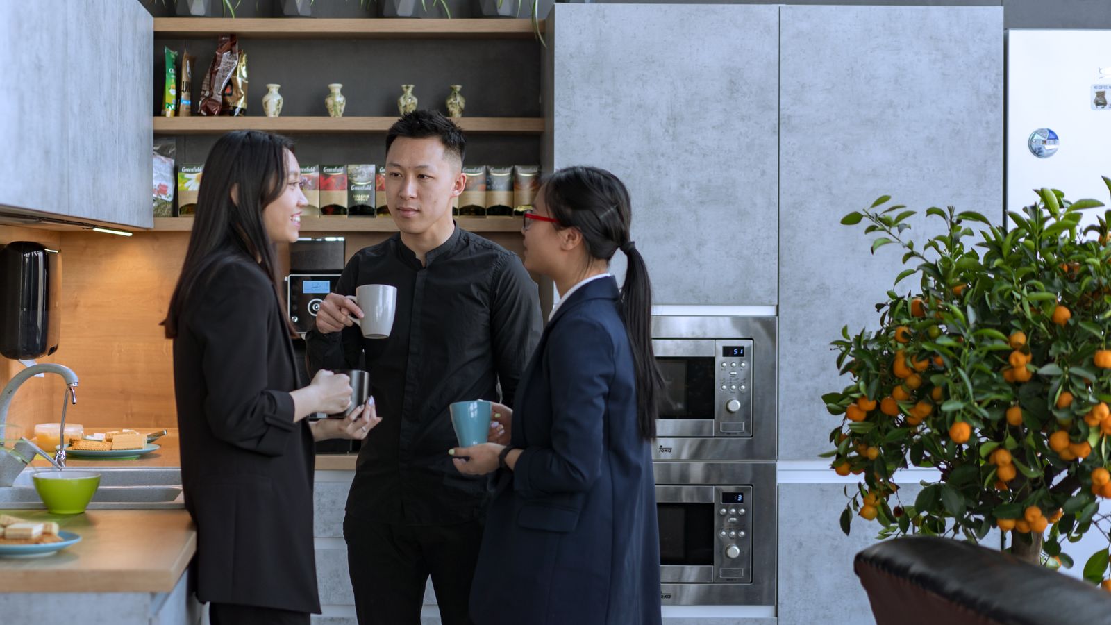 Three coworkers having a coffee break in an office kitchen