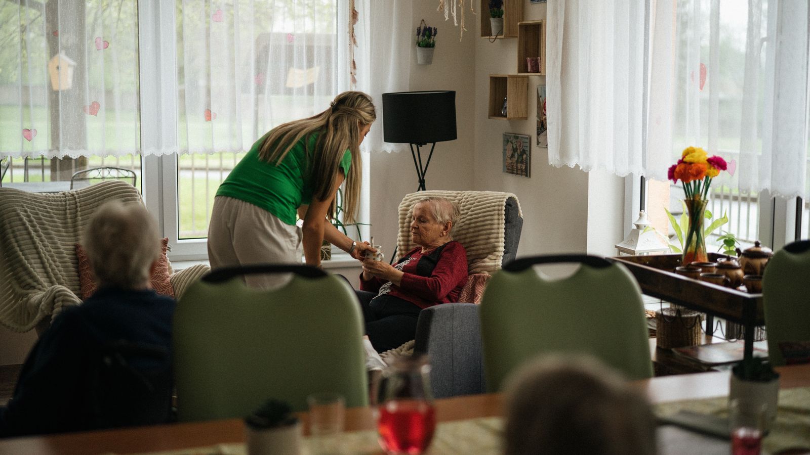 Caregiver helping elderly residents in a care home lounge